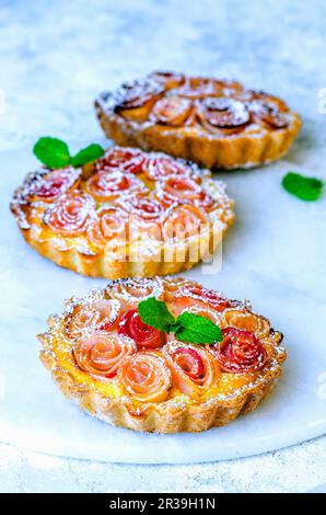 Poncer les mini-tartes avec des roses faites de tranches de pomme Banque D'Images