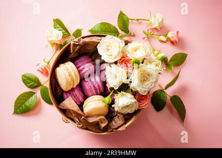 Boîte avec de délicieux macarons lumineux et des fleurs Banque D'Images