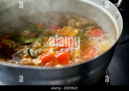 Préparation d'une soupe Tom Yum aux champignons, au poulet, à la citronnelle, aux piments, aux feuilles de caffir et aux tomates Banque D'Images