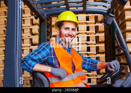 Un employé souriant qui conduit le chariot élévateur à fourche dans l'entrepôt. Concept de l'industrie du bois. Banque D'Images