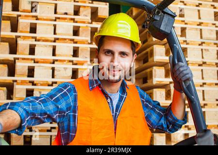 Workman porte un casque de protection, un gilet et des gants. Travailleur debout près du chariot élévateur à fourche dans l'entrepôt. Banque D'Images