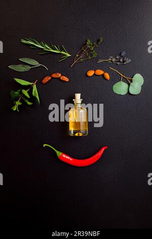 Visage souriant à base d'herbes et bouteille d'huile essentielle sur fond noir, vue sur le dessus, plat Banque D'Images