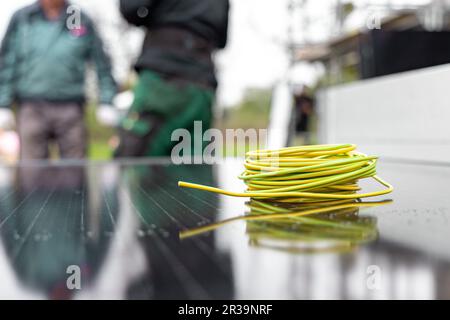 Une bobine de câble électrique sur un panneau solaire avec des techniciens en arrière-plan Banque D'Images