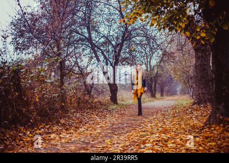 Femme marchant dans le parc d'automne. La fille élégante porte une veste en cuir noir, une robe jaune et un foulard à l'extérieur. Banque D'Images