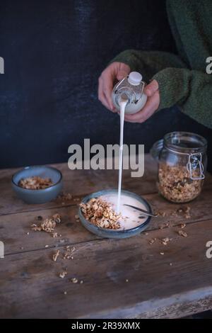 Une personne versant du lait dans un bol de muesli Banque D'Images