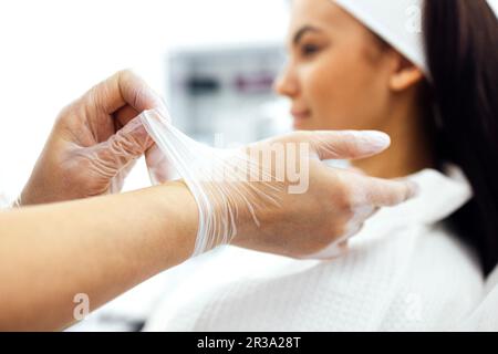 Gros plan des mains des femmes portant des gants médicaux transparents. Les dermatologues ou les cosmétologues commencent les procédures dans un salon de spa ou une clinique. Client flou Banque D'Images