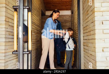 Les jeunes parents voient leurs enfants adorables à l'école. Maman, papa, fille et fils souriants descendent les marches de la terrasse de leur maison. Garçon et fille moi Banque D'Images