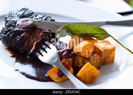 Beignets dans de la sauce au vin rouge avec des patates douces frites et une feuille de sauge Banque D'Images