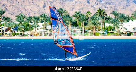 Le surfeur se promène sur le fond de la plage avec un hôtel et des palmiers en Egypte Dahab Sud Sinaï Banque D'Images