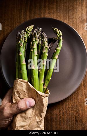 Main tenant un paquet d'asperges vertes fraîches dans un sac en papier Banque D'Images