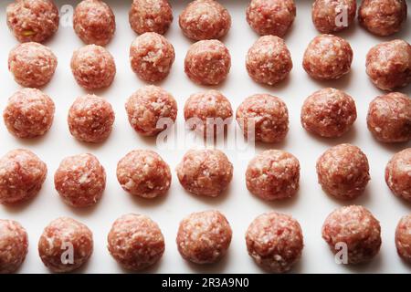 Des boulettes de viande crues fraîchement cuites sont posées sur une planche de cuisine en plastique blanc. Banque D'Images