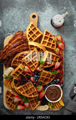 Grand bar à gaufres servi sur une planche de bois avec baies, bacon et sauce au chocolat Banque D'Images
