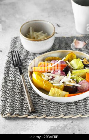 Saupoudrer de légumes mélangés avec du parmesan. Les légumes rôtis se mélangent sur l'assiette avec les couverts sur le t Banque D'Images