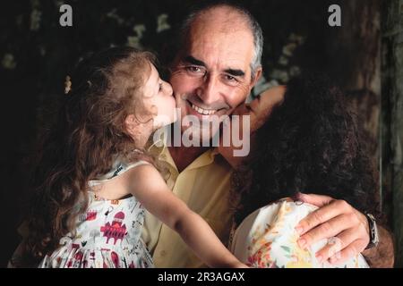 3 générations portrait de style de vie tourné - une femme et sa fille embrassant le père / grand-père regardant la caméra - blanc de famille caucasienne celebb Banque D'Images