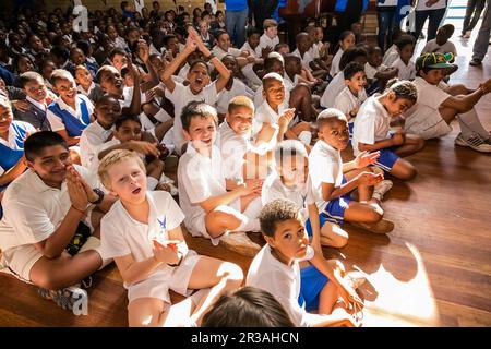 Jeunes enfants scolaires divers assis sur le plancher à une assemblée du matin Banque D'Images