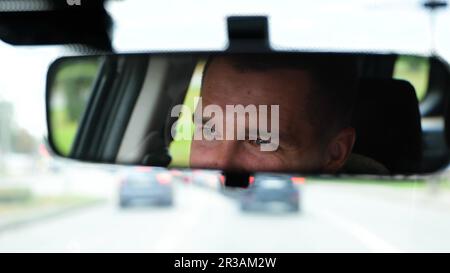 Un homme heureux conduit une voiture et souriant. Réflexion du visage dans le rétroviseur. Ralenti. Gros plan. Beau visage masculin réfléchi dans le miroir pendant la conduite Banque D'Images