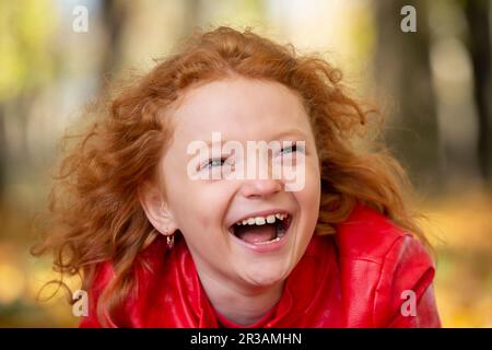 Joyeuse fille aux cheveux rouges riant avec rire avec la toile de fond d'un parc d'automne. Banque D'Images