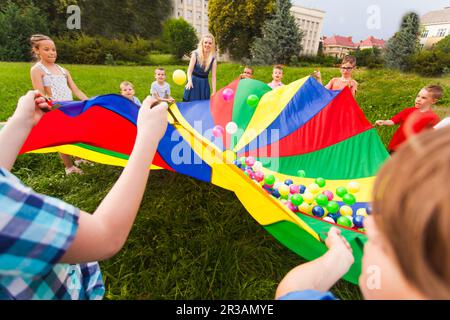 Enfants tenant un parachute arc-en-ciel avec des balles colorées Banque D'Images