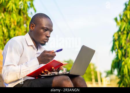 copier l'image de l'espace d'un jeune homme d'affaires beau travaillant sur un ordinateur portable et écrivant sur un bloc-notes Banque D'Images