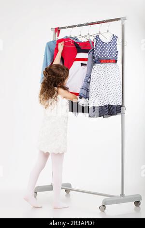 Petite femme essayant de nouveaux vêtements sur fond blanc. Une petite fille choisit la robe. Petite fille et caillot Banque D'Images