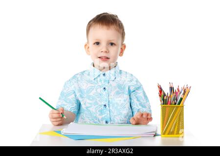 Un petit garçon souriant tire avec des crayons isolés sur fond blanc Banque D'Images