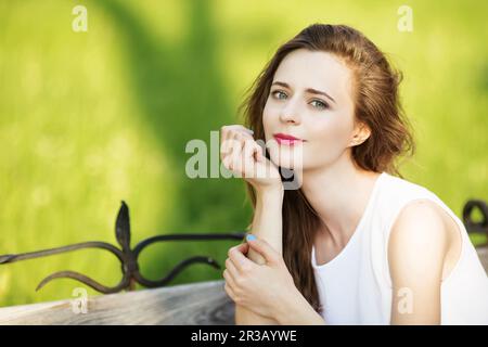 Jolie fille urbaine assise sur un banc dans un parc de la ville. Portrait d'une femme souriante heureuse. Banque D'Images