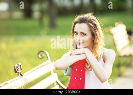 Jolie fille urbaine assise sur un banc dans un parc de la ville. Portrait d'une jeune femme souriante heureuse avec un Banque D'Images