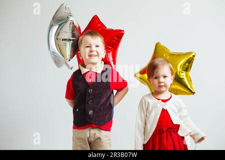 Enfants portant des ballons en forme d'étoile. Des enfants heureux jouant avec des ballons colorés en papier d'aluminium brillant ag Banque D'Images