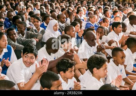 Jeunes enfants scolaires divers assis sur le plancher à une assemblée du matin Banque D'Images