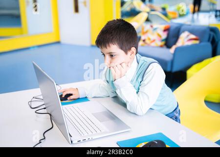 Un garçon concentré utilisant un ordinateur portable au bureau en classe informatique Banque D'Images