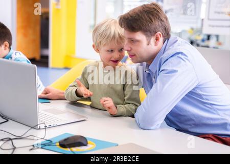 Garçon parlant à un professeur assis au bureau avec un ordinateur portable à l'école Banque D'Images