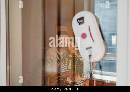 Couple souriant regardant la fenêtre d'aspiration du robot à la maison Banque D'Images