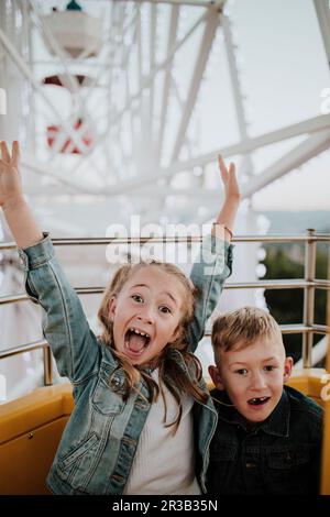 Une jeune fille joyeuse qui profite d'une balade à roulettes avec son frère dans un parc d'attractions Banque D'Images