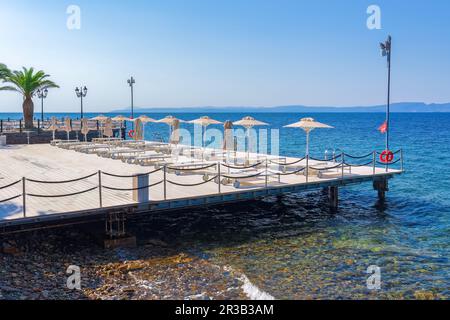 Terrasse en bois vide avec chaises et parasols au bord d'une mer bleu calme sous le soleil éclatant en été. Banque D'Images