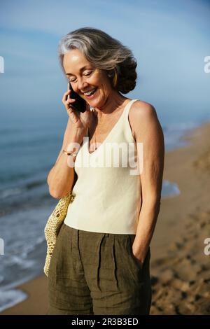 Bonne femme qui parle sur un smartphone, debout à la plage Banque D'Images