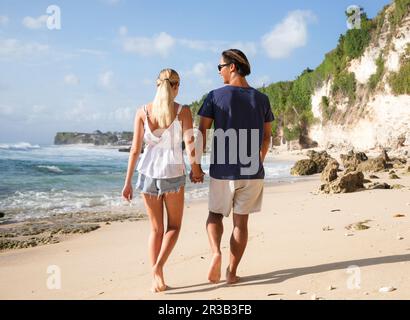 Un jeune couple heureux se tenant les mains et marchant à la plage Banque D'Images