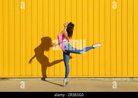 Femme portant un body montrant des mouvements de ballet devant le mur jaune Banque D'Images