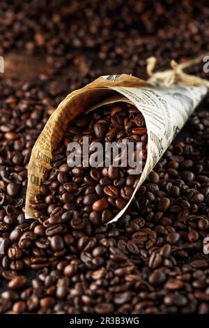 Grains de café noirs en studio. Grains de café fraîchement torréfiés dans un cône de papier Banque D'Images