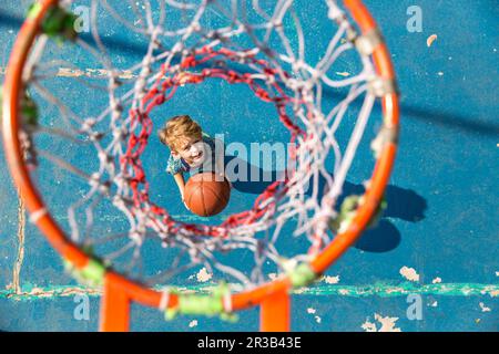 Garçon debout avec un ballon de basket-ball sous le cerceau sur le terrain de sport Banque D'Images