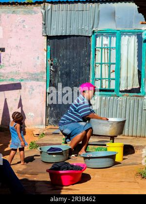 La mère et l'enfant africains lavant des vêtements dans le quartier de Soweto à faible revenu Banque D'Images