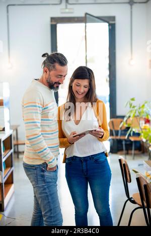 Femme souriante partageant un Tablet PC avec le propriétaire debout dans un café Banque D'Images