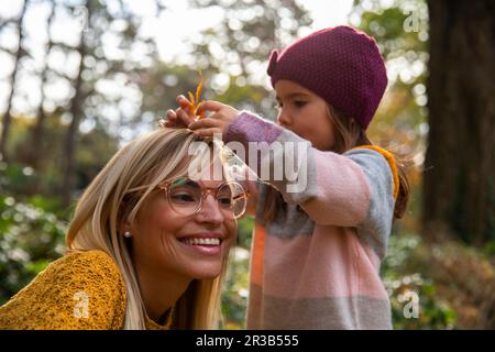 Fille mettant la feuille dans les cheveux de la mère Banque D'Images