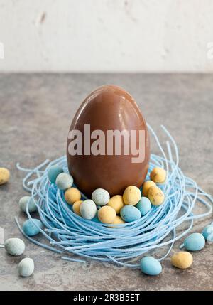 Gros œuf de Pâques au chocolat, assis dans un nid de bonbons aux myrtilles, rempli de mini œufs au chocolat Banque D'Images