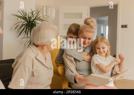 Femme âgée assise avec sa fille et ses petits-enfants et regardant un album photo à la maison Banque D'Images