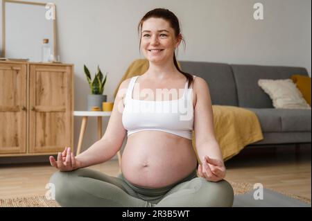 Femme enceinte souriante faisant du yoga à la maison Banque D'Images