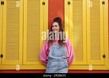 Femme souriante portant une combinaison près du mur avec des fenêtres jaunes Banque D'Images