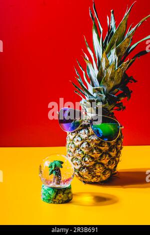Ananas avec lunettes de soleil devant un globe de neige avec un mini palmier Banque D'Images