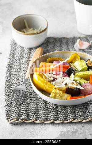 Saupoudrer de légumes mélangés avec du parmesan. Les légumes rôtis se mélangent sur l'assiette avec les couverts sur le t Banque D'Images