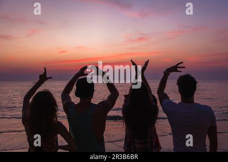 Des amis faisant l'amour signe texte avec les mains à la plage au coucher du soleil Banque D'Images