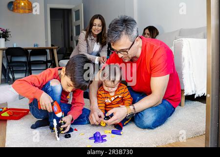 Père assis par des fils jouant avec des jouets dans la salle de séjour à la maison Banque D'Images